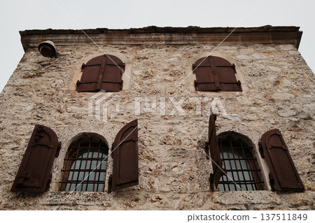 Facade of historic stone house in Mostar with wooden shutters and iron window bars. Traditional Balkan architecture showing preserved old town character 137511849