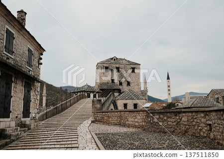 Stone path and historic buildings near the Old Bridge in Mostar with traditional houses and towers. Iconic old town scene representing Balkan history and architecture 137511850