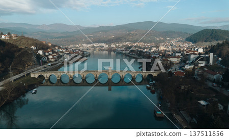 Aerial view of the historic Mehmed Pasha Sokolovic Bridge crossing the Drina River in Visegrad, Bosnia and Herzegovina. Timeless Ottoman architecture meets calm river landscape Aerial view of the historic Mehmed Pasha Sokolovic Bridge crossing the Drina River in Visegrad, Bosnia and Herzegovina. Timeless Ottoman architecture meets calm river landscape 137511856