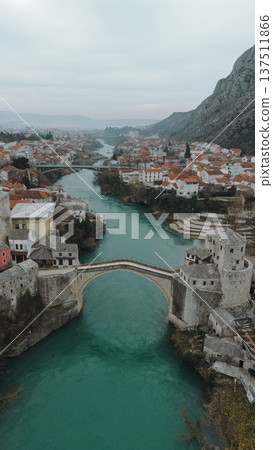 Aerial view of the historic stone bridge over the Neretva River in Mostar, with old town architecture, turquoise water, and surrounding mountains under an overcast sky. Amazing Bosnia and Herzegovina Aerial view of the historic stone bridge over the Neretva River in Mostar, with old town architecture, turquoise water, and surrounding mountains under an overcast sky. Amazing Bosnia and Herzegovina 137511866