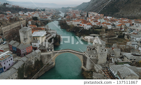 Aerial view of the historic stone bridge over the Neretva River in Mostar, with old town architecture, turquoise water, and surrounding mountains under an overcast sky. Amazing Bosnia and Herzegovina Aerial view of the historic stone bridge over the Neretva River in Mostar, with old town architecture, turquoise water, and surrounding mountains under an overcast sky. Amazing Bosnia and Herzegovina 137511867