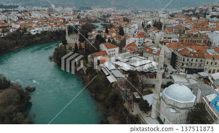 Aerial view of Mostar with turquoise Neretva River flowing through the historic old town. Stone mosque minarets and red roofs reflect the layered cultural heritage of Bosnia and Herzegovina 137511873
