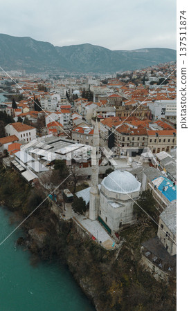 Aerial view of Mostar with turquoise Neretva River flowing through the historic old town. Stone mosque minarets and red roofs reflect the layered cultural heritage of Bosnia and Herzegovina 137511874