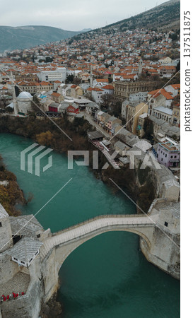 Aerial view of the historic stone bridge over the Neretva River in Mostar, with old town architecture, turquoise water, and surrounding mountains under an overcast sky. Amazing Bosnia and Herzegovina Aerial view of the historic stone bridge over the Neretva River in Mostar, with old town architecture, turquoise water, and surrounding mountains under an overcast sky. Amazing Bosnia and Herzegovina 137511875