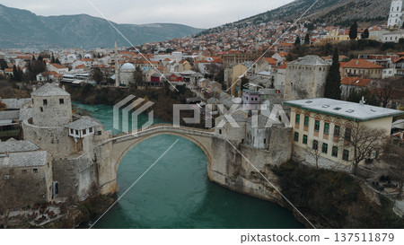 Aerial view of the historic stone bridge over the Neretva River in Mostar, with old town architecture, turquoise water, and surrounding mountains under an overcast sky. Amazing Bosnia and Herzegovina Aerial view of the historic stone bridge over the Neretva River in Mostar, with old town architecture, turquoise water, and surrounding mountains under an overcast sky. Amazing Bosnia and Herzegovina 137511879