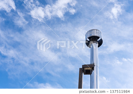 Stainless steel chimney pipe against a blue sky with clouds. Metal exhaust flue ventilation system on rooftop. Copy space for text 137511984