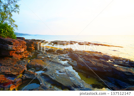 Sunset over sea on evening in coastal. Waves at rocks shore. Sunset over calm ocean water 137512147