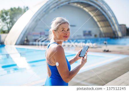 Diabetic senior woman checking glucose on her phone before swimming. Diabetic senior woman checking glucose on her phone before swimming. 137512245
