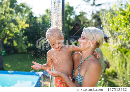 Mother showering under outdoor shower with little son. Mother showering under outdoor shower with little son. 137512282