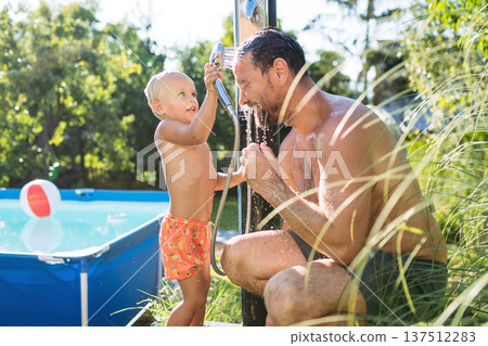 Son and father under shower by the pool on sunny summer day. Son and father under shower by the pool on sunny summer day. 137512283