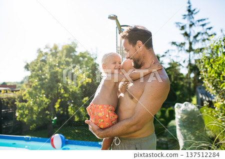 Son and father under shower by the pool on sunny summer day. Son and father under shower by the pool on sunny summer day. 137512284