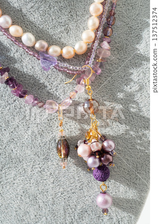 trendy author necklace with amethyst and earrings with different colors pearls around white background. fashion and handmade concept trendy author necklace with amethyst and earrings with different colors pearls around white background. fashion and handmade concept 137512374
