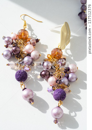 trendy author amethyst earrings with different colors pearls around white background. fashion and handmade concept. macro trendy author amethyst earrings with different colors pearls around white background. fashion and handmade concept. macro 137512376