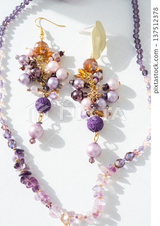 trendy author necklace with amethyst and earrings with different colors pearls around white background. fashion and handmade concept trendy author necklace with amethyst and earrings with different colors pearls around white background. fashion and handmade concept 137512378