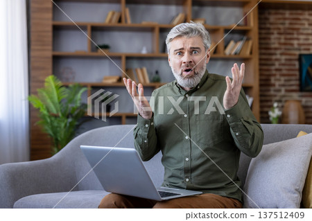 Senior man sitting on a sofa, looking surprised and frustrated at his laptop, experiencing confusion or a technical problem while using online technology at home Senior man sitting on a sofa, looking surprised and frustrated at his laptop, experiencing confusion or a technical problem while using online technology at home 137512409