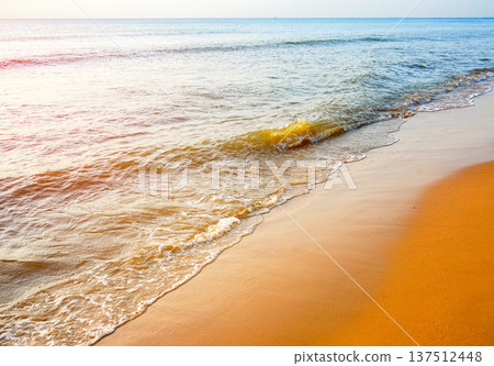 Tranquil seascape on sunset background. Soft sandy shore with warm. Waves at shoreline. 137512448