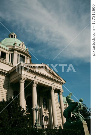 National Assembly building with classical columns and bronze sculptures in front of the entrance under a clear blue sky in Belgrade 137512600