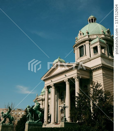 National Assembly building with classical columns and bronze sculptures in front of the entrance under a clear blue sky in Belgrade National Assembly building with classical columns and bronze sculptures in front of the entrance under a clear blue sky in Belgrade 137512604