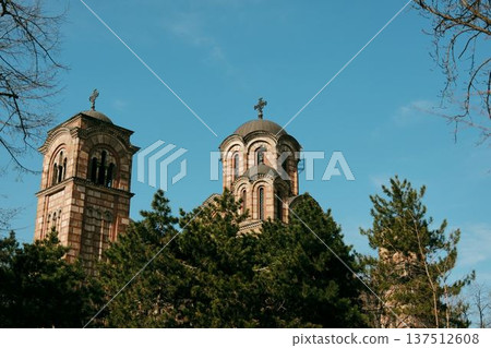 Saint Mark Church with striped brick facade and bell tower rising against a clear blue sky framed by pine branches in Belgrade Saint Mark Church with striped brick facade and bell tower rising against a clear blue sky framed by pine branches in Belgrade 137512608
