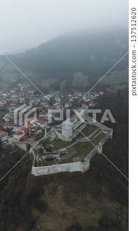 Aerial view of Travnik Fortress overlooking the town and surrounding hills, showing historic stone walls, green courtyards and misty mountain landscape from above. Amazing Bosnia and Herzegovina 137512620