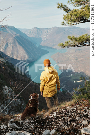A woman stands on a cliff with an Australian Shepherd above the Drina River canyon at Banjska Stena in Tara National Park, Serbia. Concept travel, hiking with pets, freedom, outdoor lifestyle A woman stands on a cliff with an Australian Shepherd above the Drina River canyon at Banjska Stena in Tara National Park, Serbia. Concept travel, hiking with pets, freedom, outdoor lifestyle 137512661