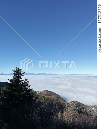 View from the hills above Sarajevo with dense clouds covering the city below and distant mountain ridges under clear blue sky. Calm winter landscape above the fog View from the hills above Sarajevo with dense clouds covering the city below and distant mountain ridges under clear blue sky. Calm winter landscape above the fog 137512896