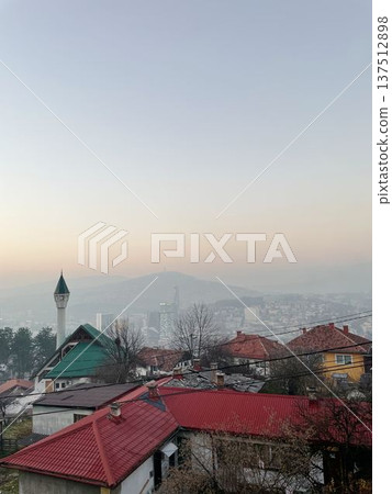 City view of Sarajevo with residential rooftops, mosque minaret, and distant urban skyline under soft evening haze. Calm Balkan atmosphere with layered cityscape City view of Sarajevo with residential rooftops, mosque minaret, and distant urban skyline under soft evening haze. Calm Balkan atmosphere with layered cityscape 137512898
