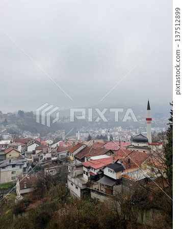 Panoramic view of Travnik city with dense rooftops, mosque minaret, and hills in the background. Overcast winter scene showing Balkan town atmosphere Panoramic view of Travnik city with dense rooftops, mosque minaret, and hills in the background. Overcast winter scene showing Balkan town atmosphere 137512899