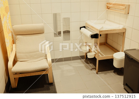 Clean baby care room with a changing table, chair, paper dispenser, and tiled walls, designed for comfort and hygiene in public spaces Clean baby care room with a changing table, chair, paper dispenser, and tiled walls, designed for comfort and hygiene in public spaces 137512915
