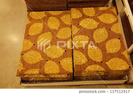 Stacked coir doormats with yellow lemon patterns displayed in a retail store, showing textured natural fibers and colorful graphic design Stacked coir doormats with yellow lemon patterns displayed in a retail store, showing textured natural fibers and colorful graphic design 137512917