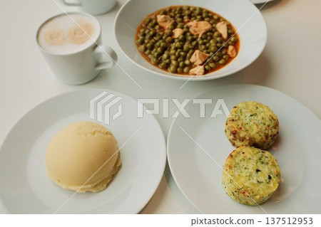 Close view of green pea stew with chicken pieces served on white plates with mashed potatoes and vegetable patties. Warm homemade lunch concept, casual dining atmosphere 137512953