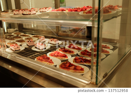 Strawberry cheesecake slices arranged on plates inside a bakery display case. Fresh fruit dessert concept for cafe menu and pastry showcase Strawberry cheesecake slices arranged on plates inside a bakery display case. Fresh fruit dessert concept for cafe menu and pastry showcase 137512958