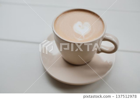 Cup of coffee with heart latte art on a white table. Minimal morning scene showing warmth, comfort, cafe culture, and calm lifestyle moments 137512978