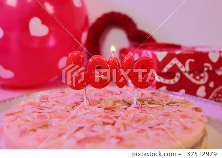 Romantic cake topped with almond flakes and a lit red love candle, surrounded by heart decorations and gift wrapping. Festive dessert concept for Valentine celebration and romantic occasions Romantic cake topped with almond flakes and a lit red love candle, surrounded by heart decorations and gift wrapping. Festive dessert concept for Valentine celebration and romantic occasions 137512979