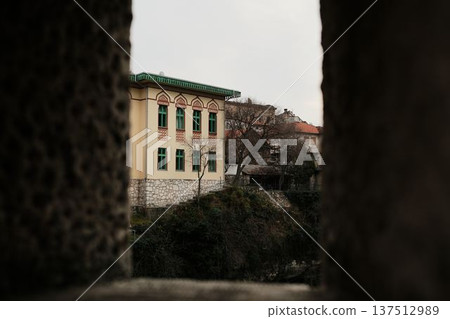View through stone opening toward historic building in Mostar old town. Framed urban scene highlighting traditional Balkan architecture and cultural heritage 137512989