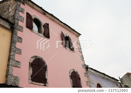 Pink historic house in Mostar old town with stone window frames and wooden shutters. Traditional Balkan architecture showing preserved heritage and calm urban atmosphere 137512993