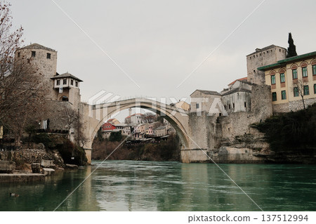 Iconic stone bridge of Mostar spanning the Neretva River with historic towers and old town buildings. Famous Balkan landmark representing medieval architecture and cultural heritage 137512994