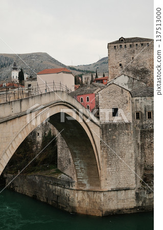 Close view of the historic stone bridge in Mostar with old town buildings and river below. Iconic Balkan architecture showing medieval heritage and cultural identity 137513000