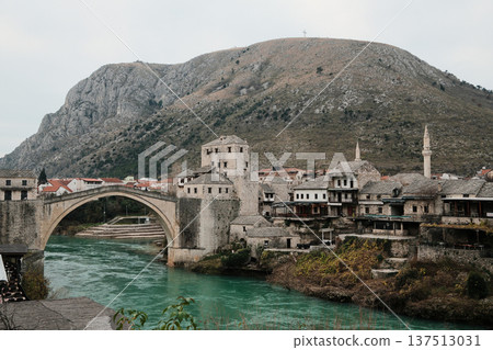 Historic stone bridge and old town of Mostar spanning the turquoise Neretva River, surrounded by traditional buildings and mountains. Iconic Balkan landmark representing culture, heritage, and travel Historic stone bridge and old town of Mostar spanning the turquoise Neretva River, surrounded by traditional buildings and mountains. Iconic Balkan landmark representing culture, heritage, and travel 137513031