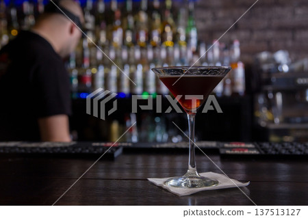 A dark alcoholic cocktail in a martini glass served on a napkin on a bar counter A dark alcoholic cocktail in a martini glass served on a napkin on a bar counter 137513127