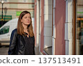 Woman standing near building wall on city street 137513491
