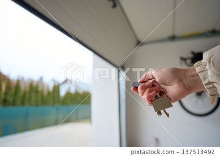 Closeup of hand holding garage remote and keys inside garage with open door Closeup of hand holding garage remote and keys inside garage with open door 137513492