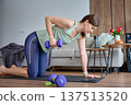Woman performs one arm dumbbell row on exercise mat in living room with smartphone nearby 137513520