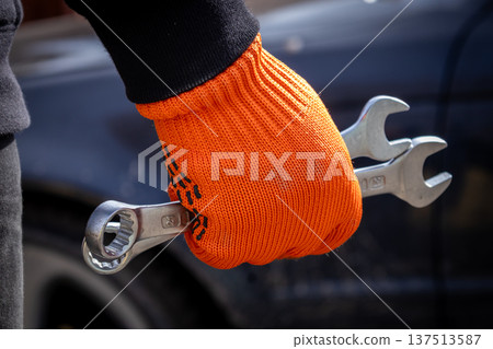 A man stands ready to fix a car with tools in hand inside a garage during the day A man stands ready to fix a car with tools in hand inside a garage during the day 137513587