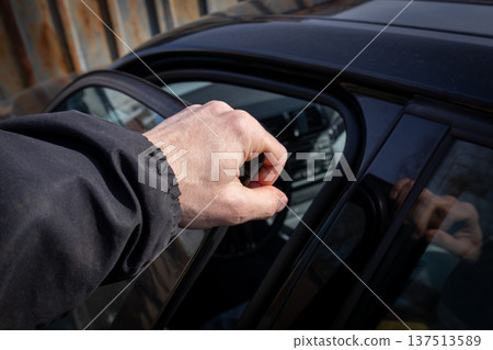 A man uses his hand to open the door of a modern car in a city parking area during daylight hours A man uses his hand to open the door of a modern car in a city parking area during daylight hours 137513589