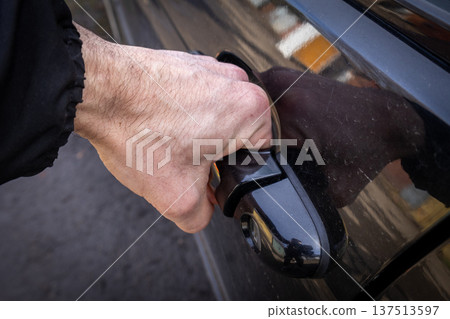 Man reaches for the handle to open a car door in a parking area during daylight hours Man reaches for the handle to open a car door in a parking area during daylight hours 137513597