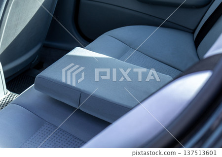 A back seat area is shown with comfortable car seats. A center armrest is placed on one of the seats during daytime A back seat area is shown with comfortable car seats. A center armrest is placed on one of the seats during daytime 137513601