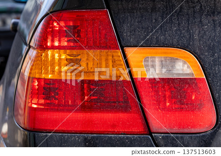 Close view of a modern car's taillight featuring red and orange sections indicating functions while parked in a lot under sunlight Close view of a modern car's taillight featuring red and orange sections indicating functions while parked in a lot under sunlight 137513603