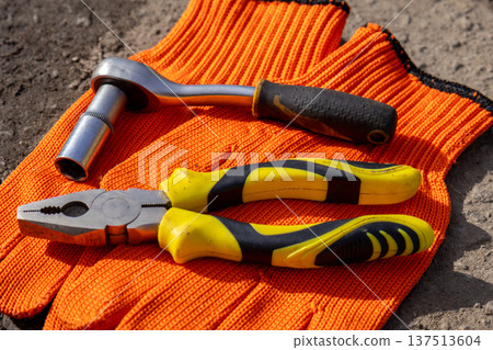 A set of tools rests on orange gloves in a workshop, showing a mixture of hand tools used in maintenance tasks 137513604