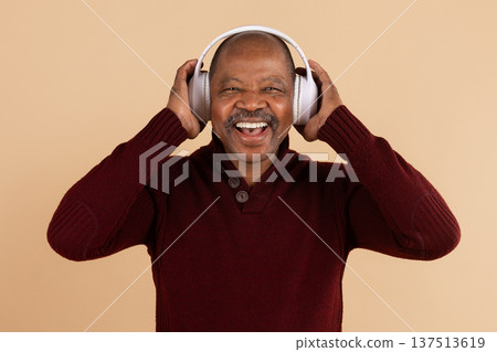 Happy mature black man adjusting wireless headphones while smiling on beige background 137513619